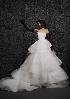 a woman in a white wedding dress standing against a black wall with her arms outstretched