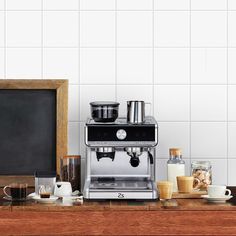 an espresso machine sitting on top of a wooden counter next to cups and saucers