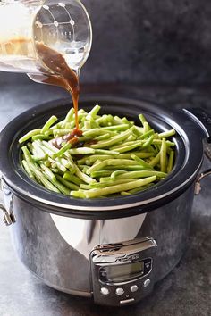 green beans are being cooked in an electric pressure cooker with a measuring cup pouring them into the pot