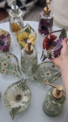 a person holding a flower in front of several glass vases with flowers on them