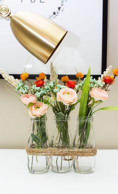 three vases filled with flowers sitting on top of a white table next to a gold lamp