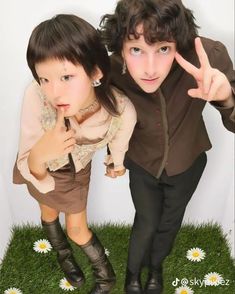 two young people standing next to each other on top of a grass covered field with daisies