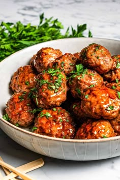 a white bowl filled with meatballs covered in sauce and garnished with parsley