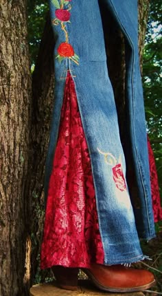 a woman's jeans with flowers on them are hanging from a tree trunk in the woods