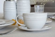 a white cup and saucer sitting on top of a table next to silverware