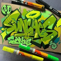 two markers are next to some graffiti on a piece of brown paper with green and yellow letters