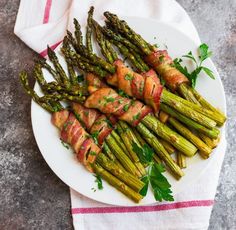 asparagus wrapped in bacon on a white plate with a red and white towel