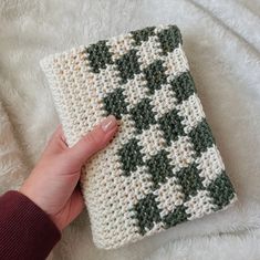 a hand is holding a crocheted square with green and white squares on it