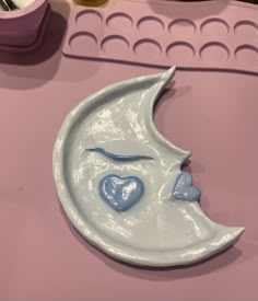 a ceramic moon with a blue heart on it's face sitting on a pink surface