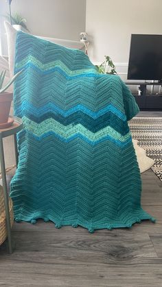 a blue crocheted blanket sitting on top of a wooden floor next to a table