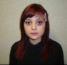 a woman with red hair and bangs standing in front of a white wall looking at the camera