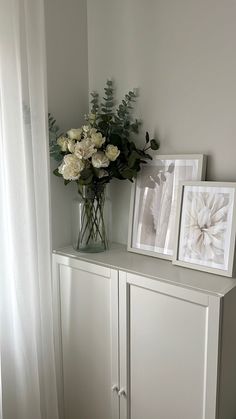 a vase with white flowers sitting on top of a cabinet next to two framed pictures