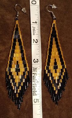 a pair of black and yellow beaded earrings next to a measuring ruler on a brown background