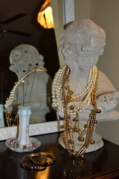 a white statue sitting on top of a table next to a mirror and some jewelry