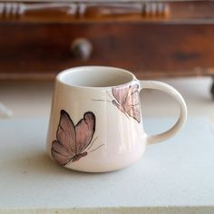 a white coffee cup with pink butterflies painted on the outside and inside, sitting on a table