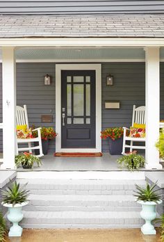 the front porch is decorated with white rocking chairs and potted plants