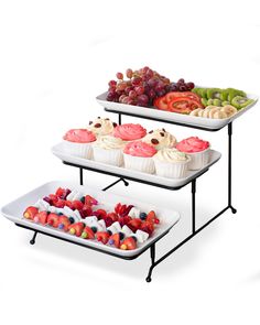 three trays filled with cupcakes and fruit on top of each other in front of a white background