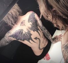 a woman with tattoos on her back is looking at herself in the mirror