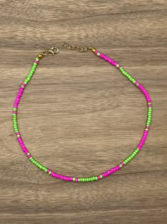 a pink, green and yellow beaded necklace on a wooden surface with a gold chain