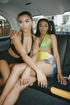 two women sitting in the back seat of a car, one with her arm around the other's shoulder