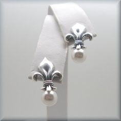 "Sterling silver fleur de lis stud earrings are accented with a glowing white Swarovski elements half-drilled pearl. Classic, beautiful and unusual. This symbol has traditionally been used to represent French royalty, and in that sense it is said to signify perfection, light, and life. Fleur de lis translates to \"flower of the lily\" in English. The earrings are about 7/8\" long (1.8 cm) from the top of the fleur de lis to the bottom of the pearl. Setting, earnuts and earring components are all Pearl Setting, French Royalty, Flower Stud, Earrings Pearl, Lily Flower, The Pearl, Earrings Sterling Silver, Silver Wedding, Wedding Earrings