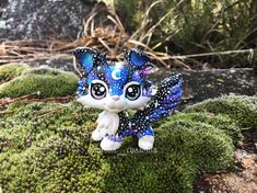 a small blue and white cat figurine sitting on top of green moss covered ground