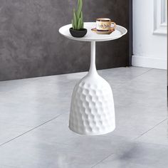 a white table with a potted plant sitting on it's side and a cup next to it