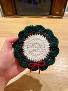 a hand holding a small crocheted ornament with red and green trim