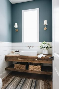 a bathroom with blue walls and white fixtures, including a wooden counter top that has baskets under the sink