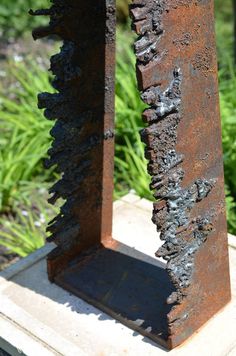 a rusted metal object sitting on top of a cement block in front of some grass