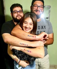 two men and a woman with tattoos on their arms hugging each other in front of a mirror