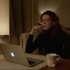 a woman sitting at a table with an apple laptop in front of her and a coffee mug