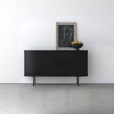 a black cabinet sitting in front of a white wall next to a bowl of fruit