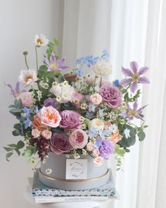 a bouquet of flowers is sitting on top of a table next to a book and window