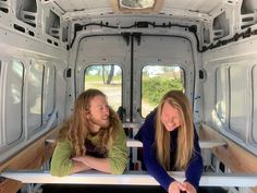 two women sitting in the back of a white van with open doors smiling at each other