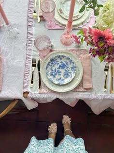 the table is set with plates, silverware and pink flowers