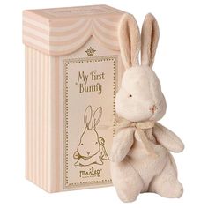 a white stuffed rabbit sitting next to a pink box with the words my first bunny on it