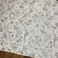 a table cloth with birds and flowers on it sitting on a wooden floor in front of a window