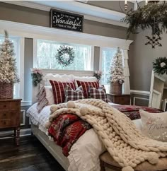 a large bed covered in blankets and pillows next to two christmas wreaths on the windowsill