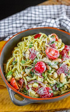 a bowl filled with pasta and vegetables on top of a wooden cutting board next to a fork