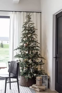 a small christmas tree in a living room next to a window with white drapes