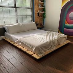 a bed sitting on top of a hard wood floor next to a window covered in blinds