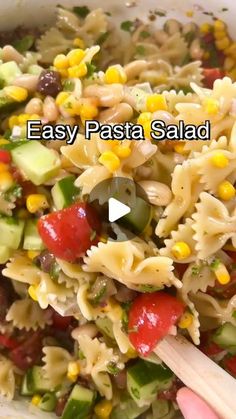 pasta salad with vegetables and olives in a white bowl being held by a wooden spoon