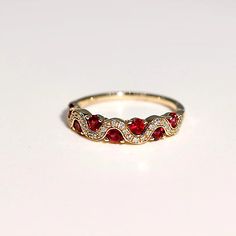 a gold ring with red and white stones on it's sides, sitting on a white surface