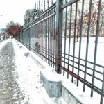 a snow covered sidewalk next to a metal fence