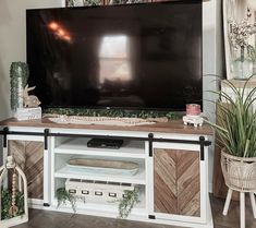 a flat screen tv sitting on top of a wooden entertainment center next to potted plants