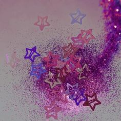 purple and blue glitter stars are scattered on a white surface with pink sparkles in the background