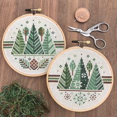 two cross stitch hoops sitting on top of a wooden table next to a pair of scissors