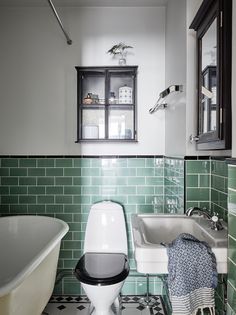 a white toilet sitting next to a bath tub in a bathroom with green tiles on the walls