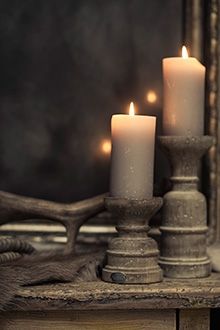 three lit candles sitting on top of a wooden table next to a mirror with lights in the background